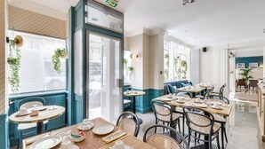 A restaurant with round tables, chairs, and a view of the street. - Hotel Passy Eiffel (Paris)