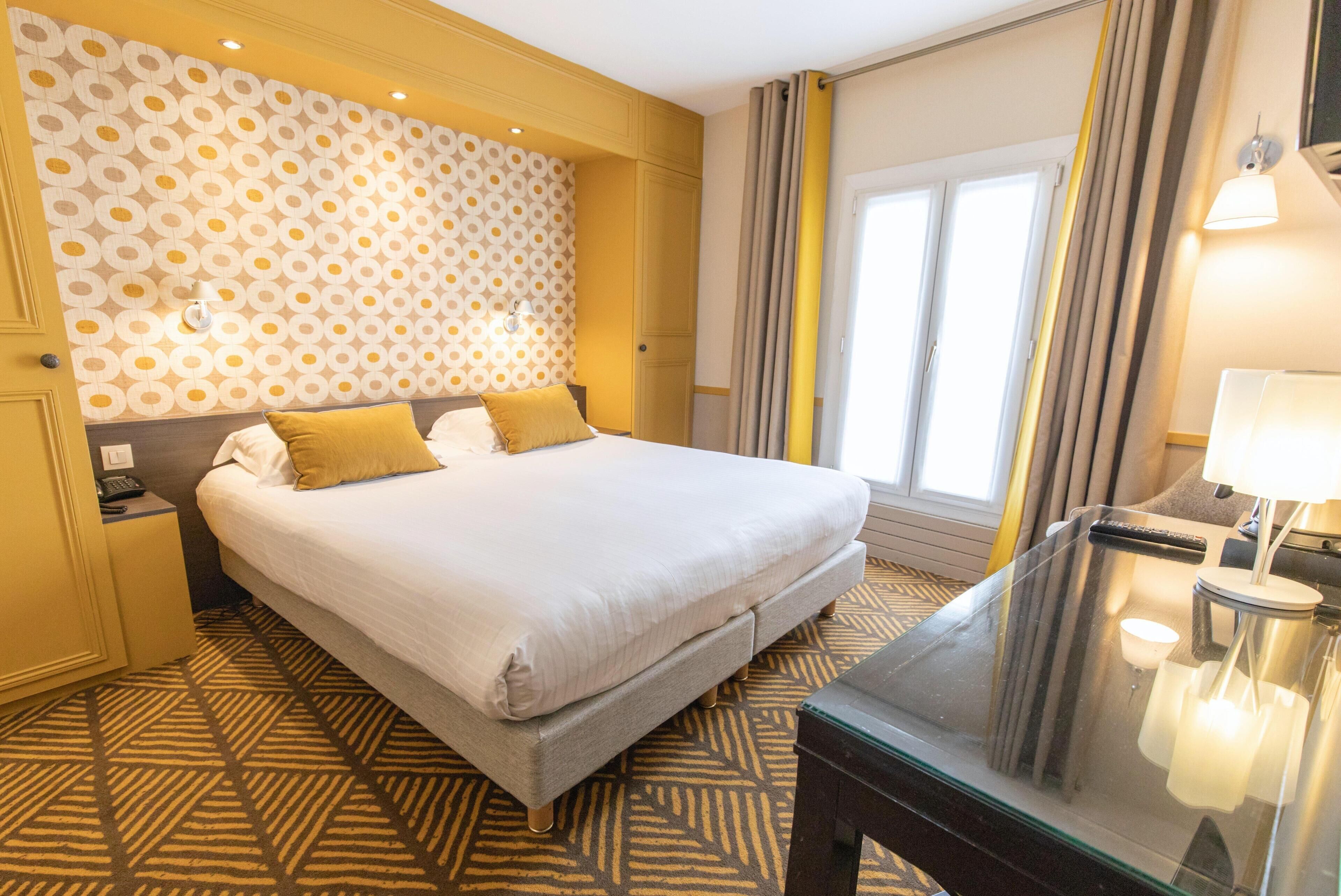 Habitación de hotel con una cama grande, una mesita de noche, un espejo y un papel tapiz estampado.