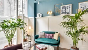 A modern living room with a teal sofa, a round coffee table, and two potted plants. - Hotel Passy Eiffel (Paris)