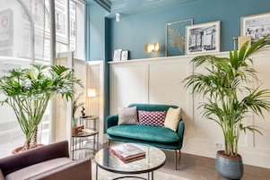 A modern living room with a teal sofa, a round coffee table, and two potted plants.