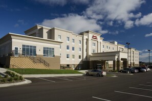 A modern hotel with a prominent entrance, a parking lot, and a clear blue sky.