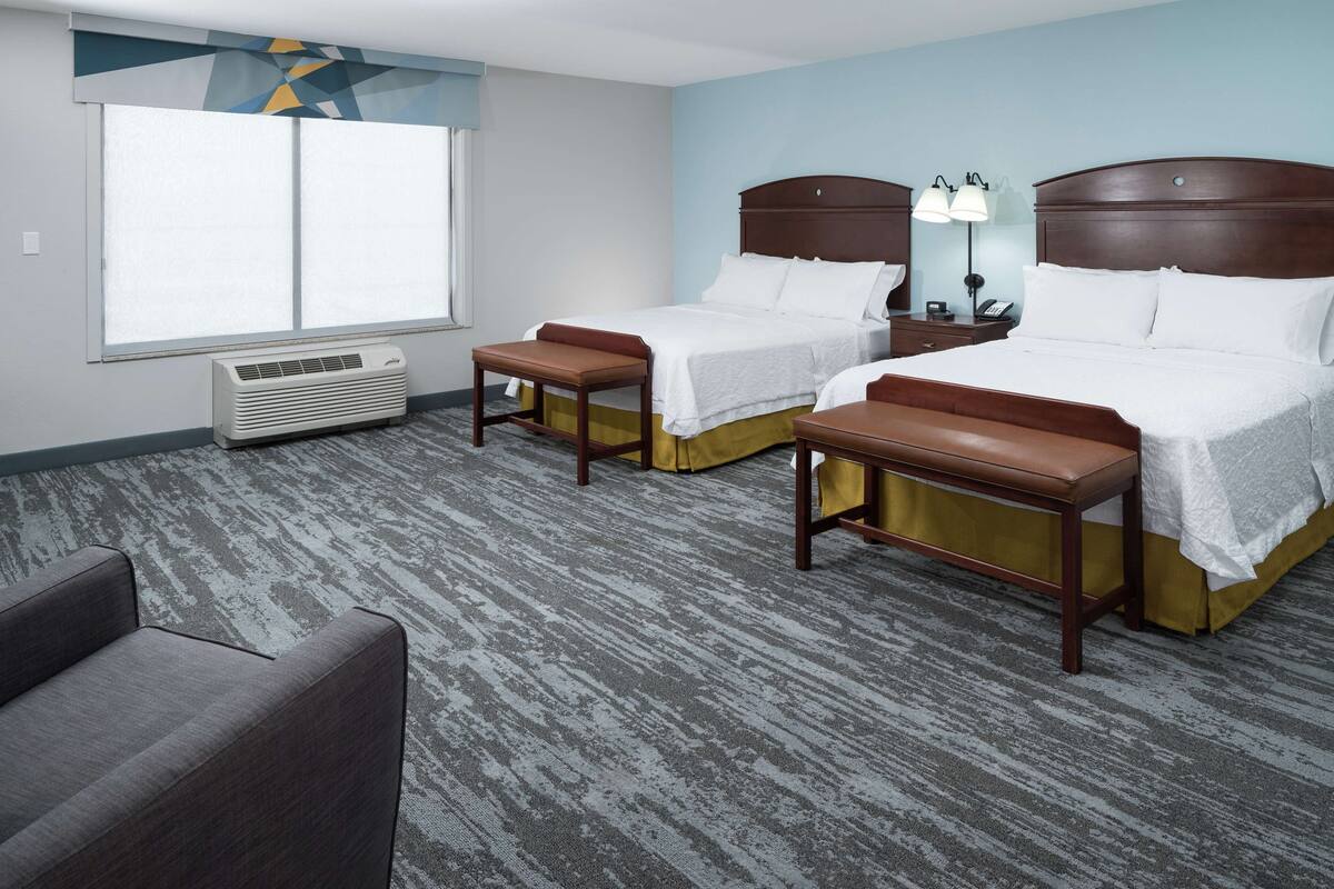 A hotel room with two beds, a desk, a chair, and a large window.