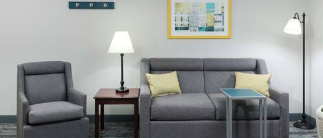 Une pièce avec un canapé gris, un fauteuil gris, une petite table, un lampadaire et un tableau abstrait encadré accroché au mur.