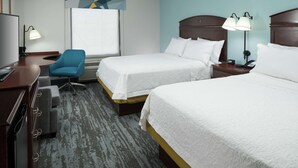 A hotel room with two beds, a desk with a computer, a chair, and a window with a view.