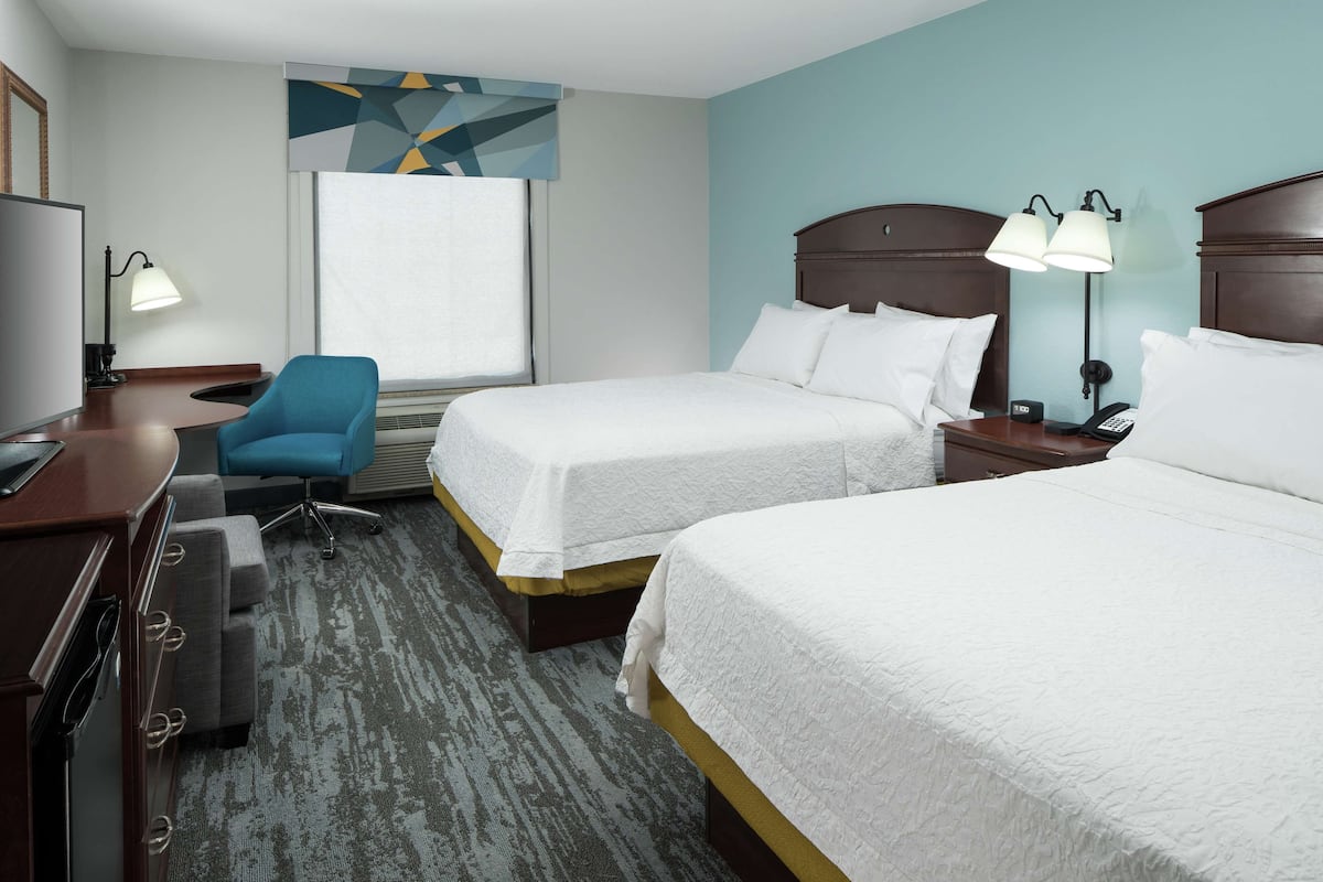 A hotel room with two beds, a desk with a computer, a chair, and a window with a view.
