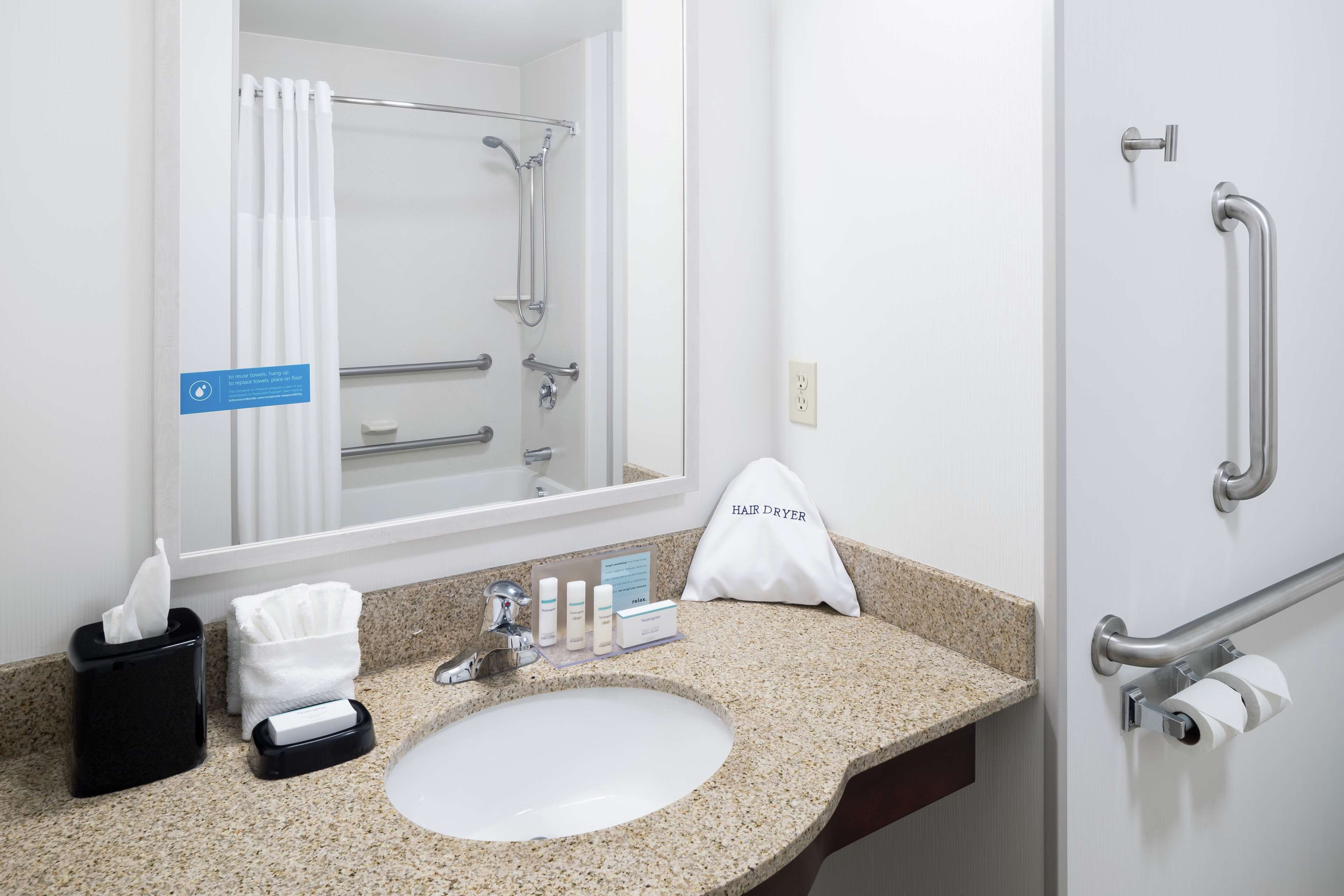 Un baño de hotel con lavabo, espejo, dispensador de toallas y un secador de pelo sobre la encimera.