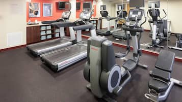 Een sportschool met loopbanden, elliptische trainers en een spiegelwand.