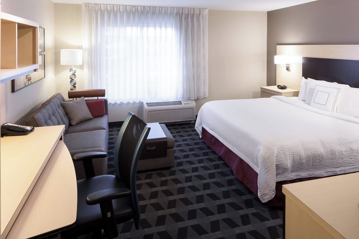 Une chambre d’hôtel avec un lit, un bureau, une chaise, un canapé, une lampe et une fenêtre avec des rideaux.