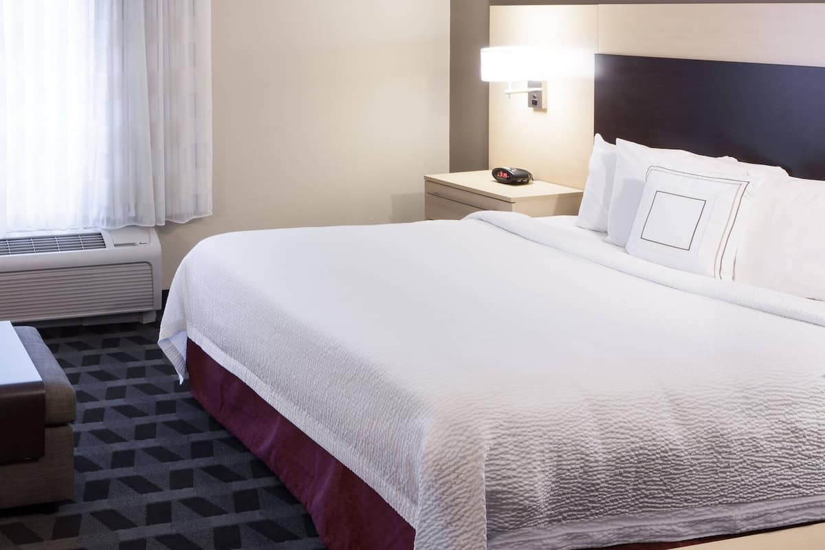 Une chambre d’hôtel avec un grand lit, une table de chevet, une petite table de nuit avec une lampe et une fenêtre avec des rideaux.