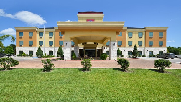 A multi-story hotel with a central entrance, a flat roof, and a landscaped front yard.
