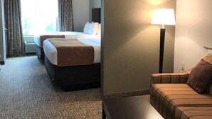 A hotel room with two beds, a desk, a lamp, and a sofa.