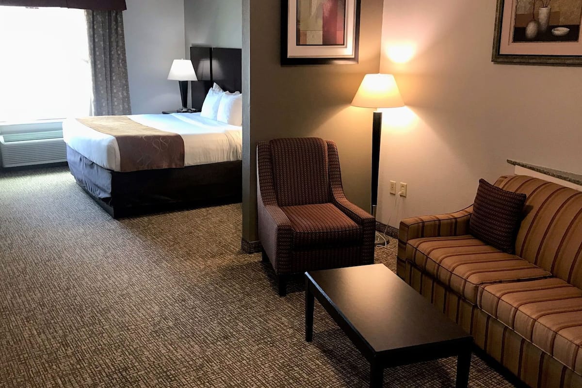 A hotel room with a bed, a chair, a sofa, a table, and two lamps.