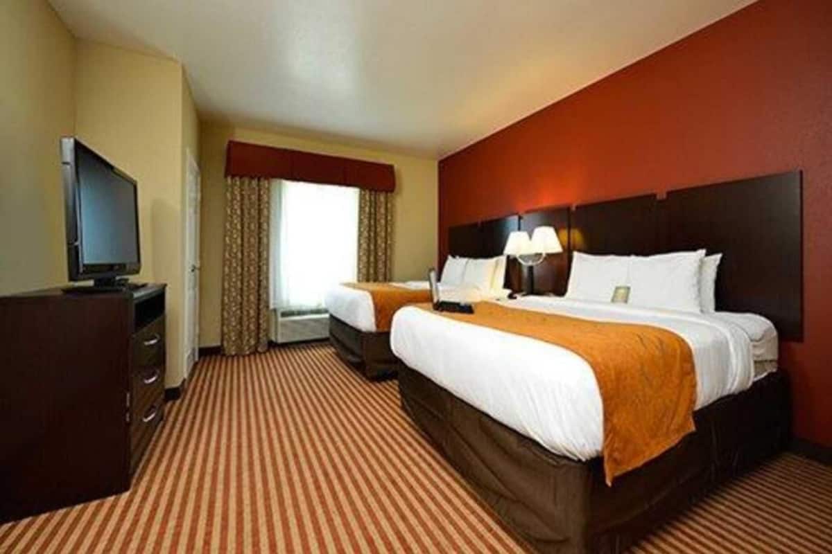 A hotel room with two beds, a television, a desk, and a window with curtains.