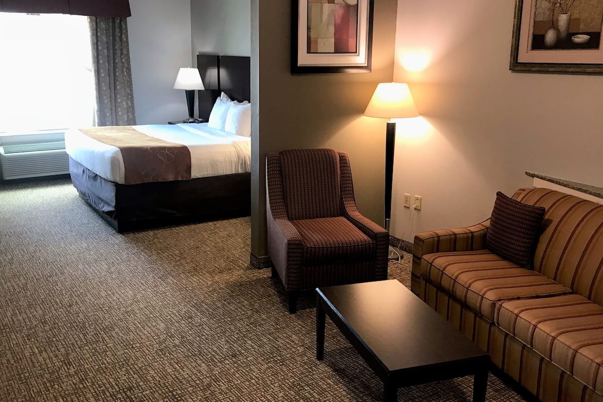 A hotel room with a bed, a chair, a sofa, a table, and a lamp.