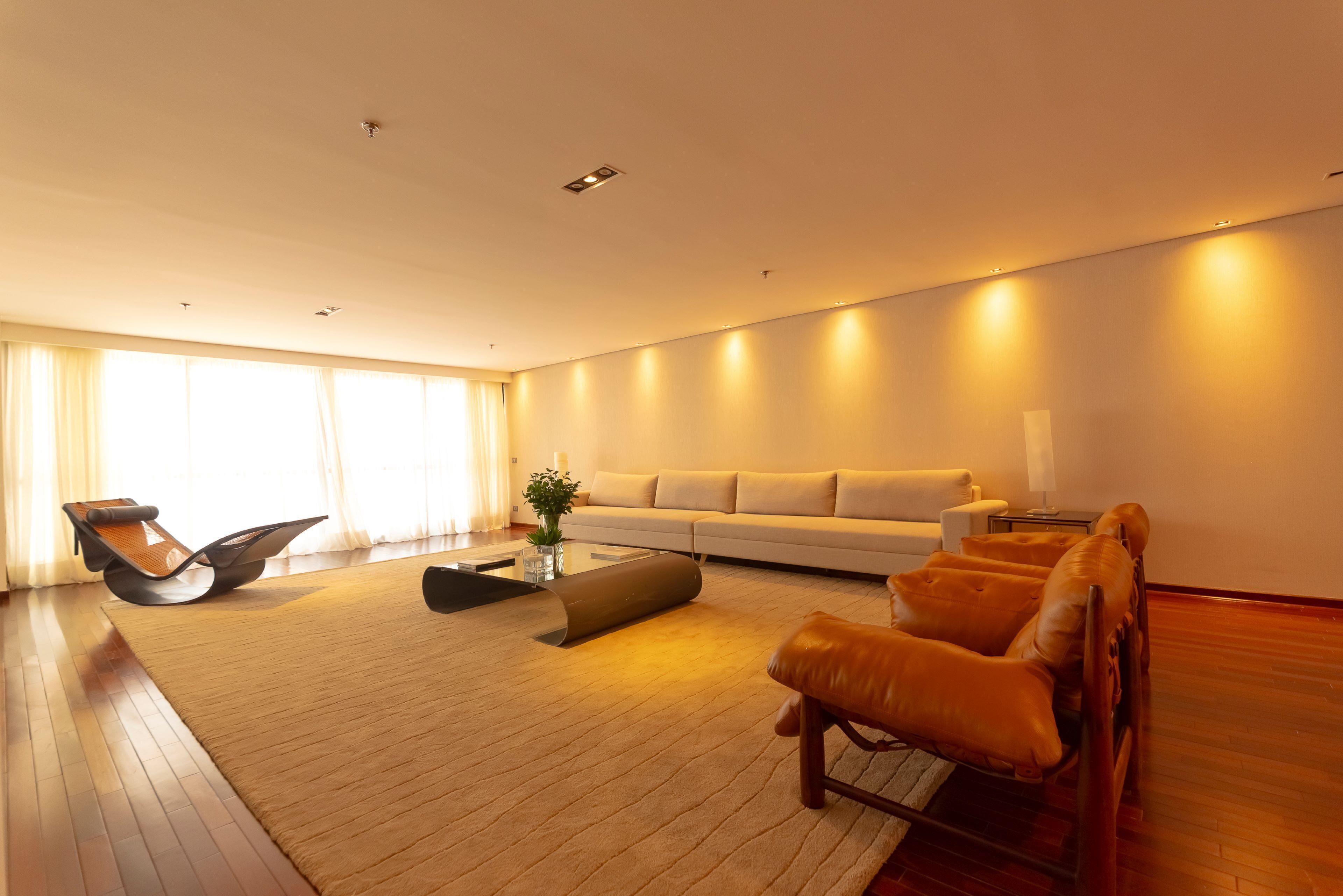 A modern living room with a sofa, leather armchairs, a coffee table, and a large window with curtains.