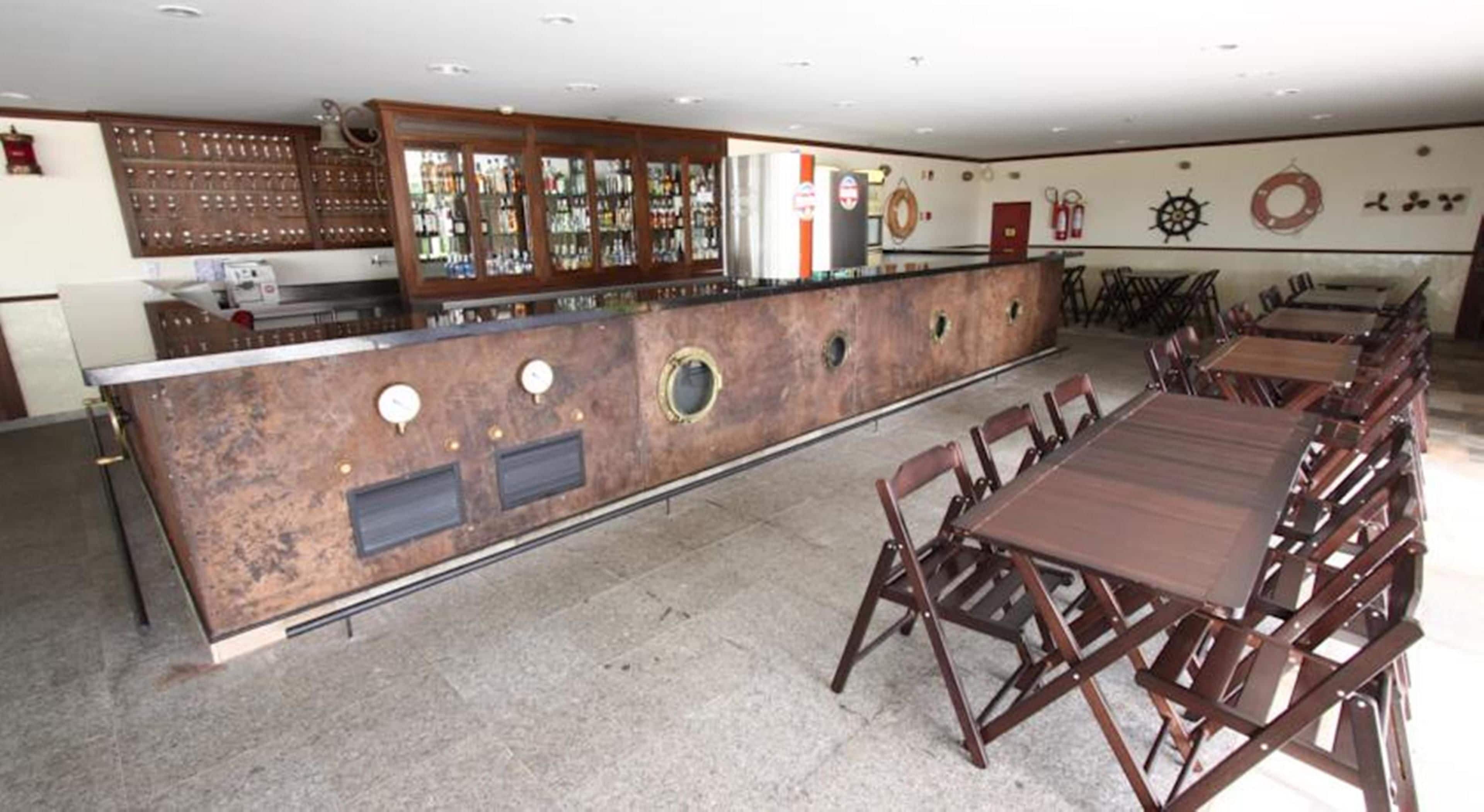 Restaurante com um balcão comprido, várias mesas e área de bar com armário de madeira e vitrine de vidro.