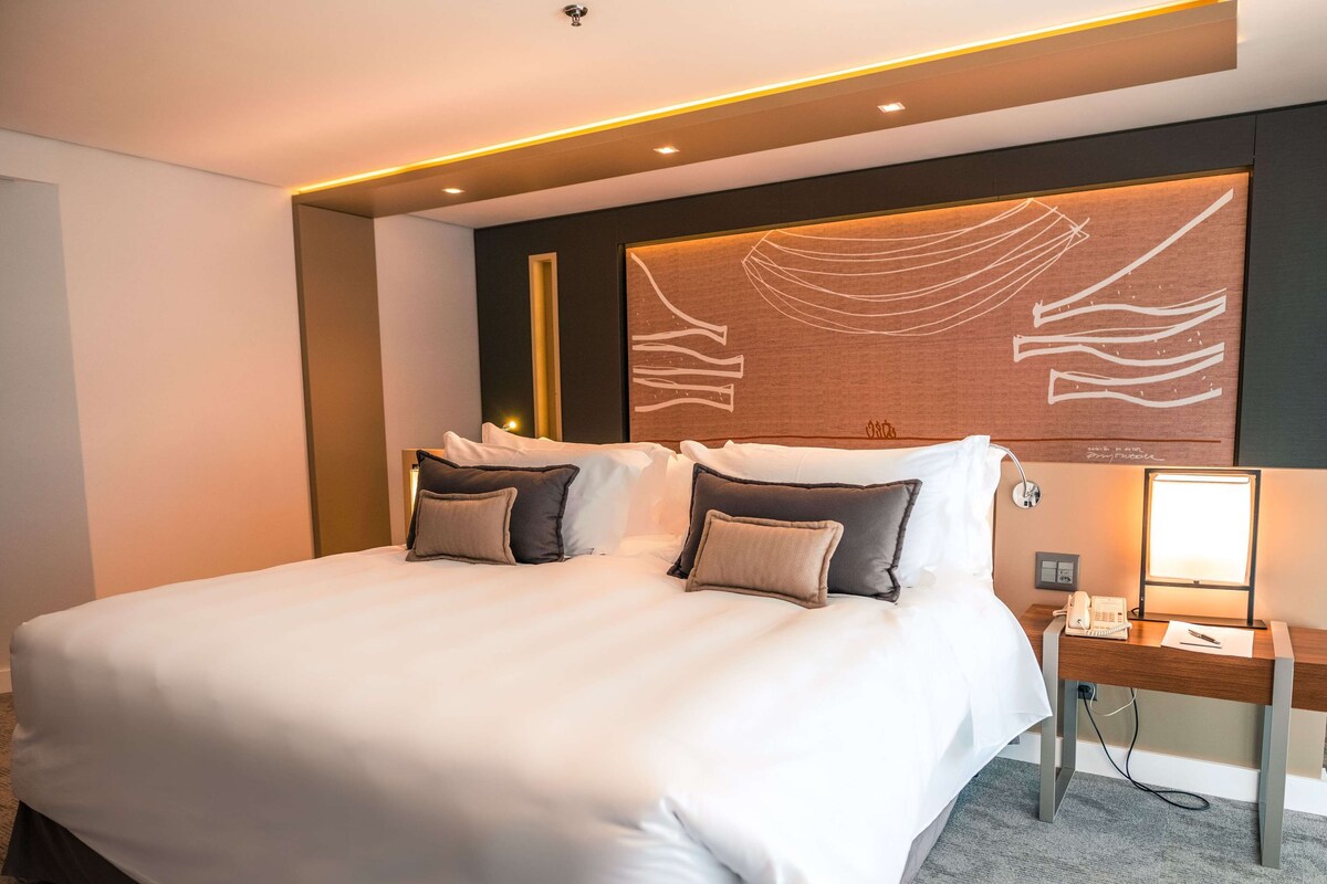 A hotel room with a large bed, a bedside table with a lamp, and a wall-mounted artwork.