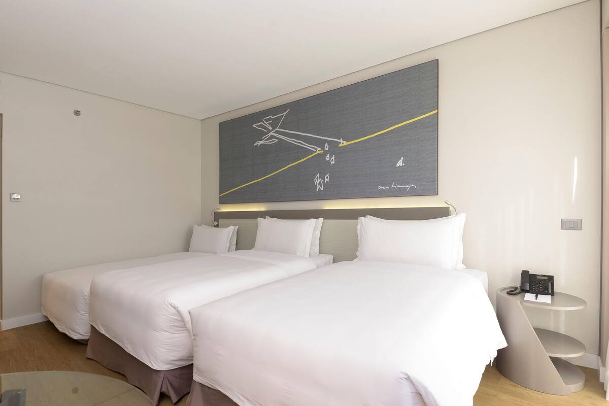 A hotel room with two beds, a modern abstract painting, a bedside table with a phone, and a small rug.