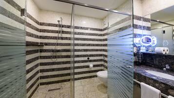 Un baño moderno con ducha de vidrio, piso de mármol y tocador con lavamanos y espejo.