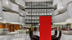 Un vestíbulo amplio con techo alto, suelo de mármol y una llamativa escultura roja.