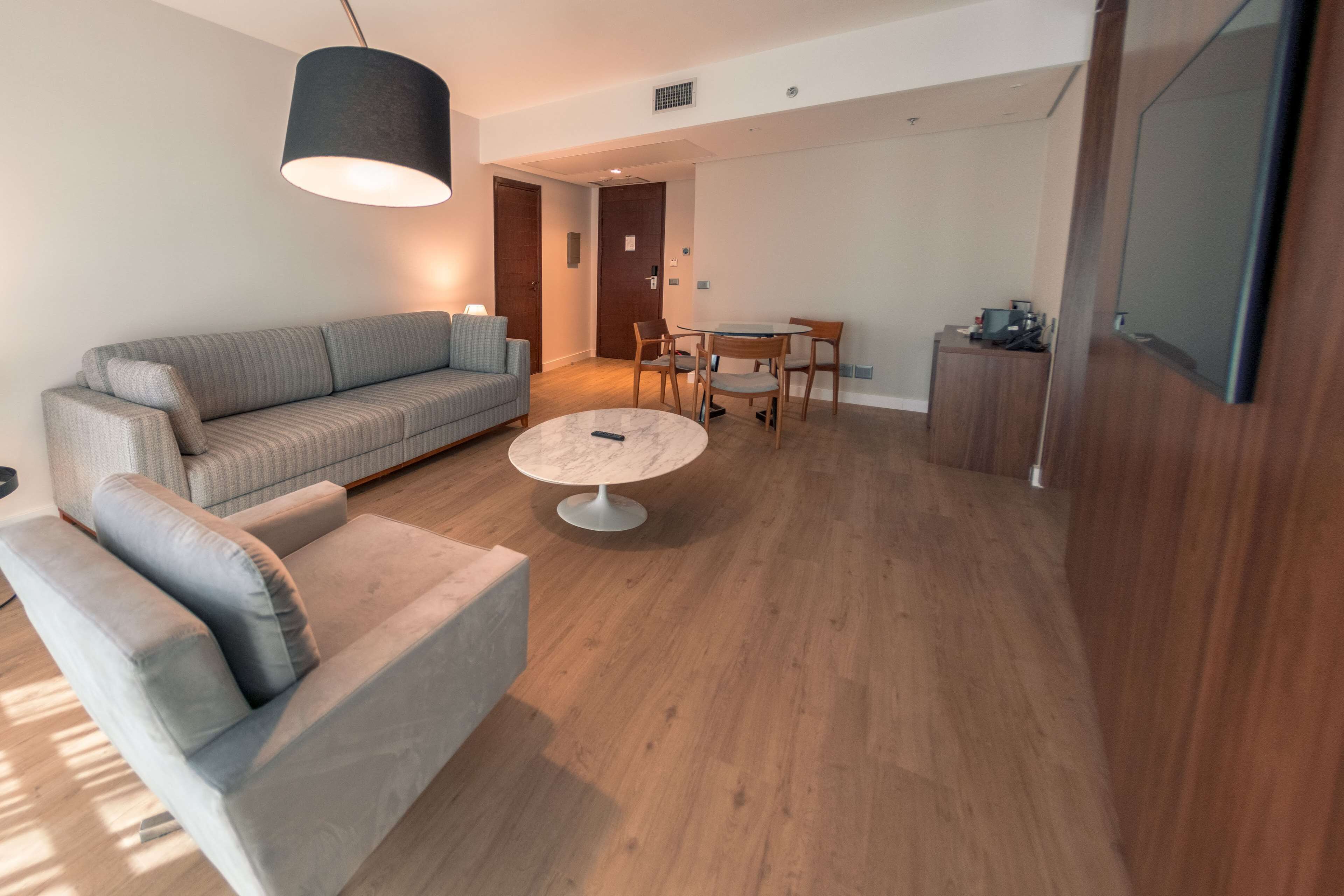 Uma sala de estar moderna com um sofá cinzento, uma mesa de centro redonda e um espaço de refeições com cadeiras e uma mesa de madeira.