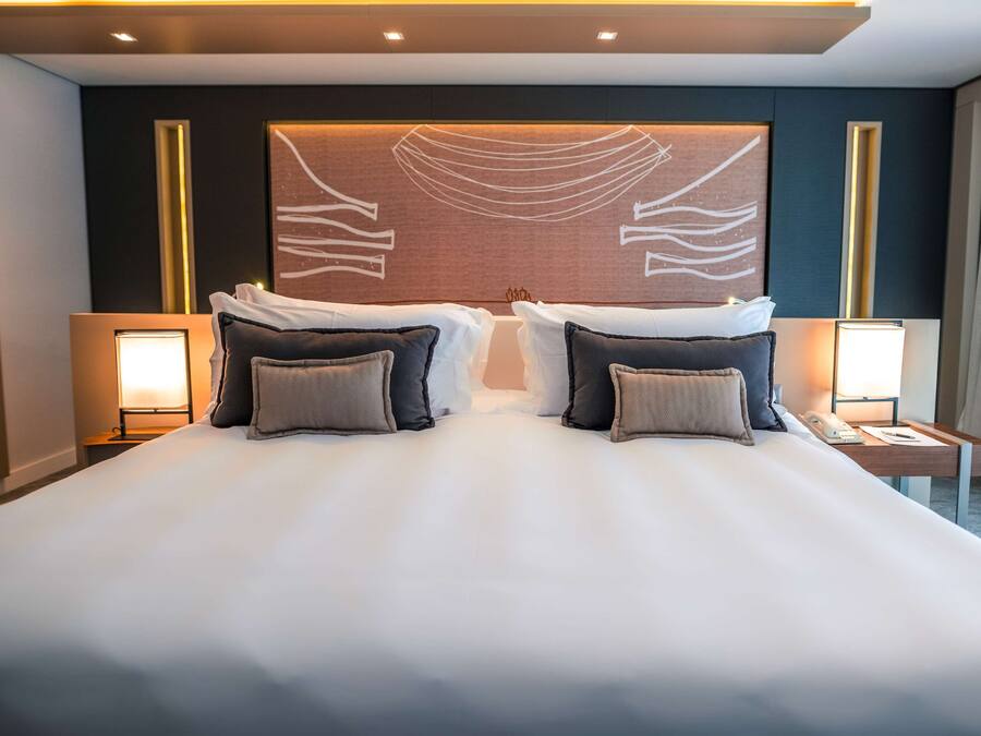 A large bed with white linens, two bedside tables, and a wall-mounted artwork.