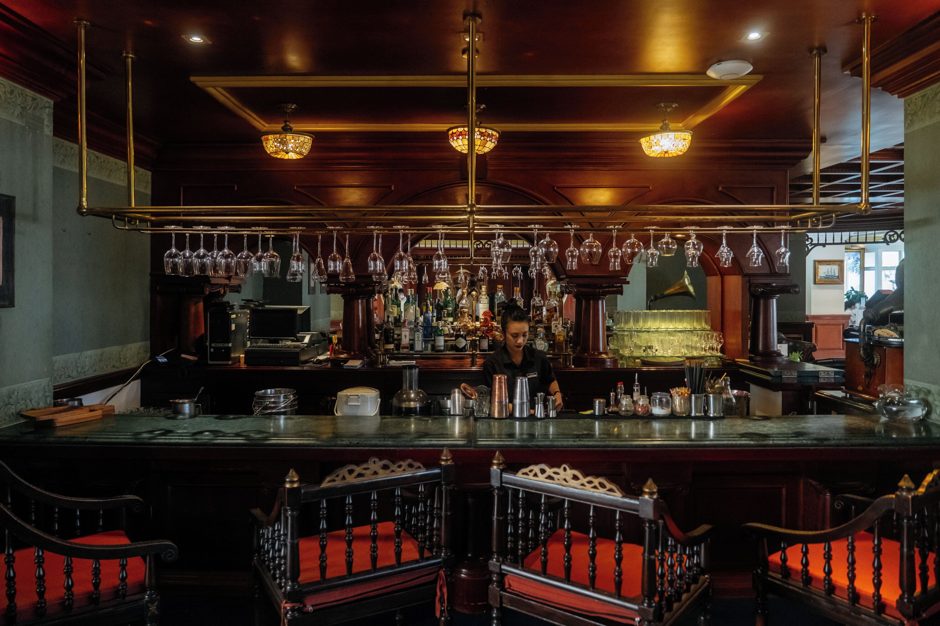 A bar area with a bartender, bar counter, and seating with red cushions.
