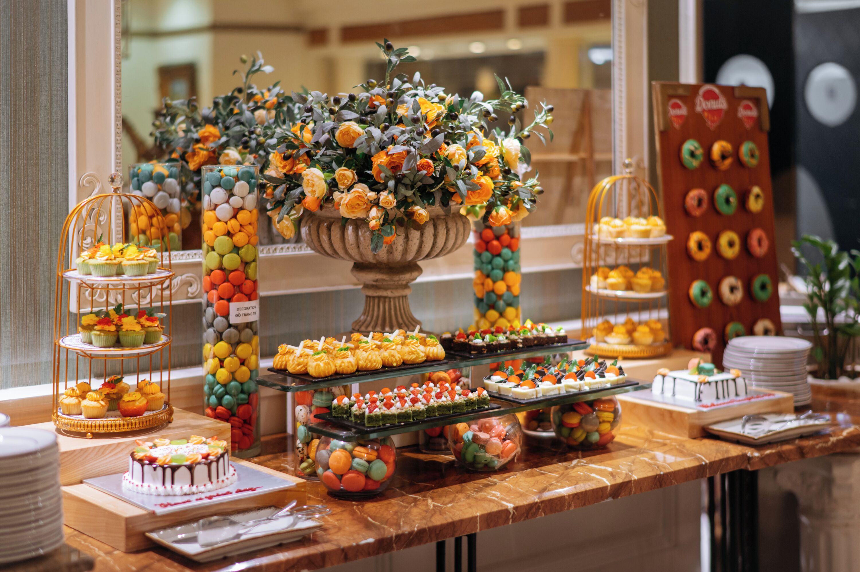 Una mesa de buffet con diversos postres, un centro de mesa floral y una exhibición de rosquillas.