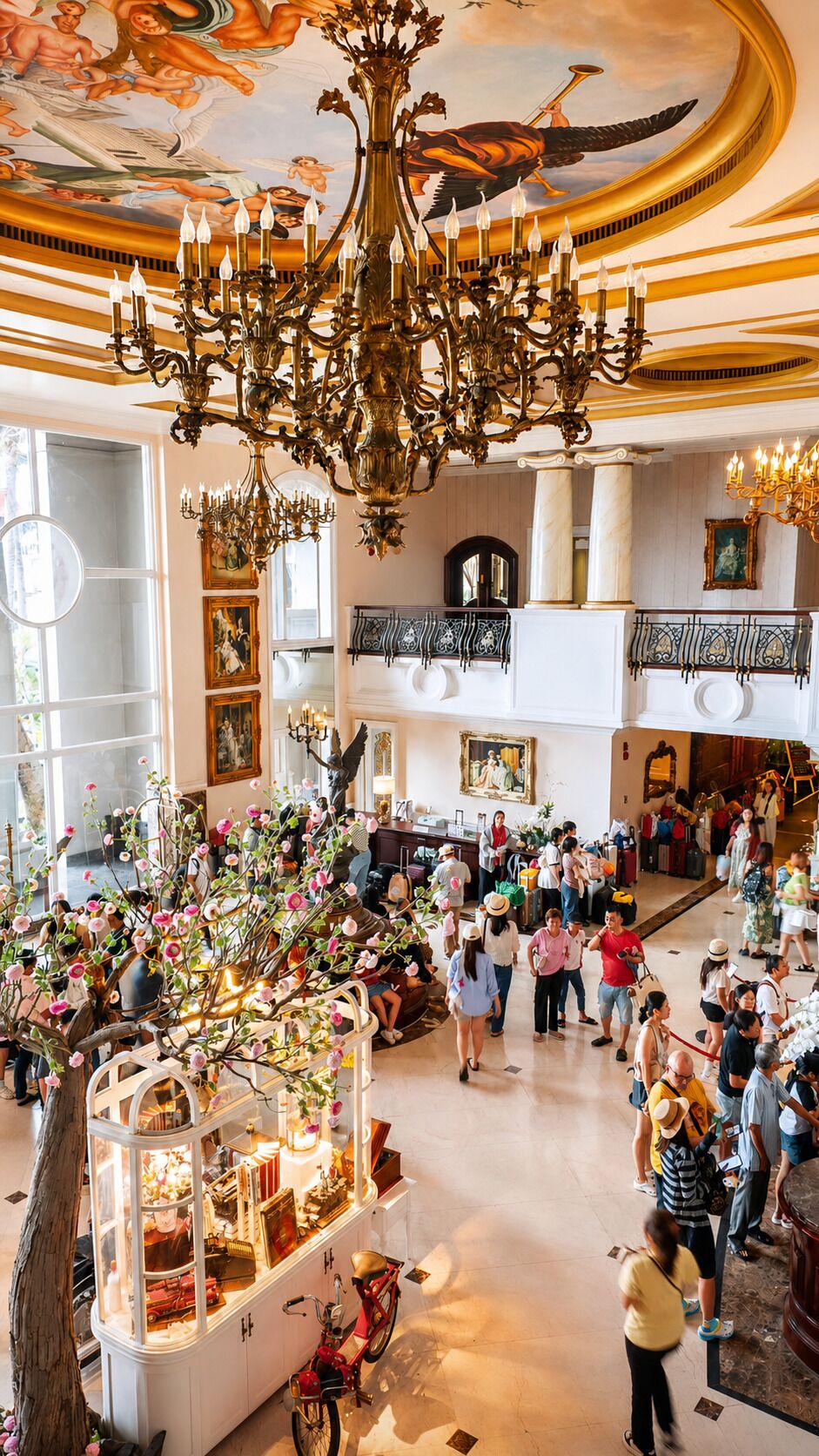 A grand lobby with a large chandelier, multiple levels, and a central floral display.