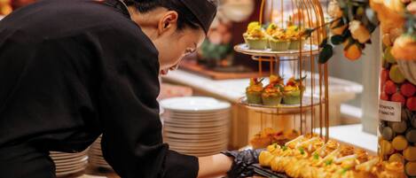 A buffet setup with various food items and a person serving.