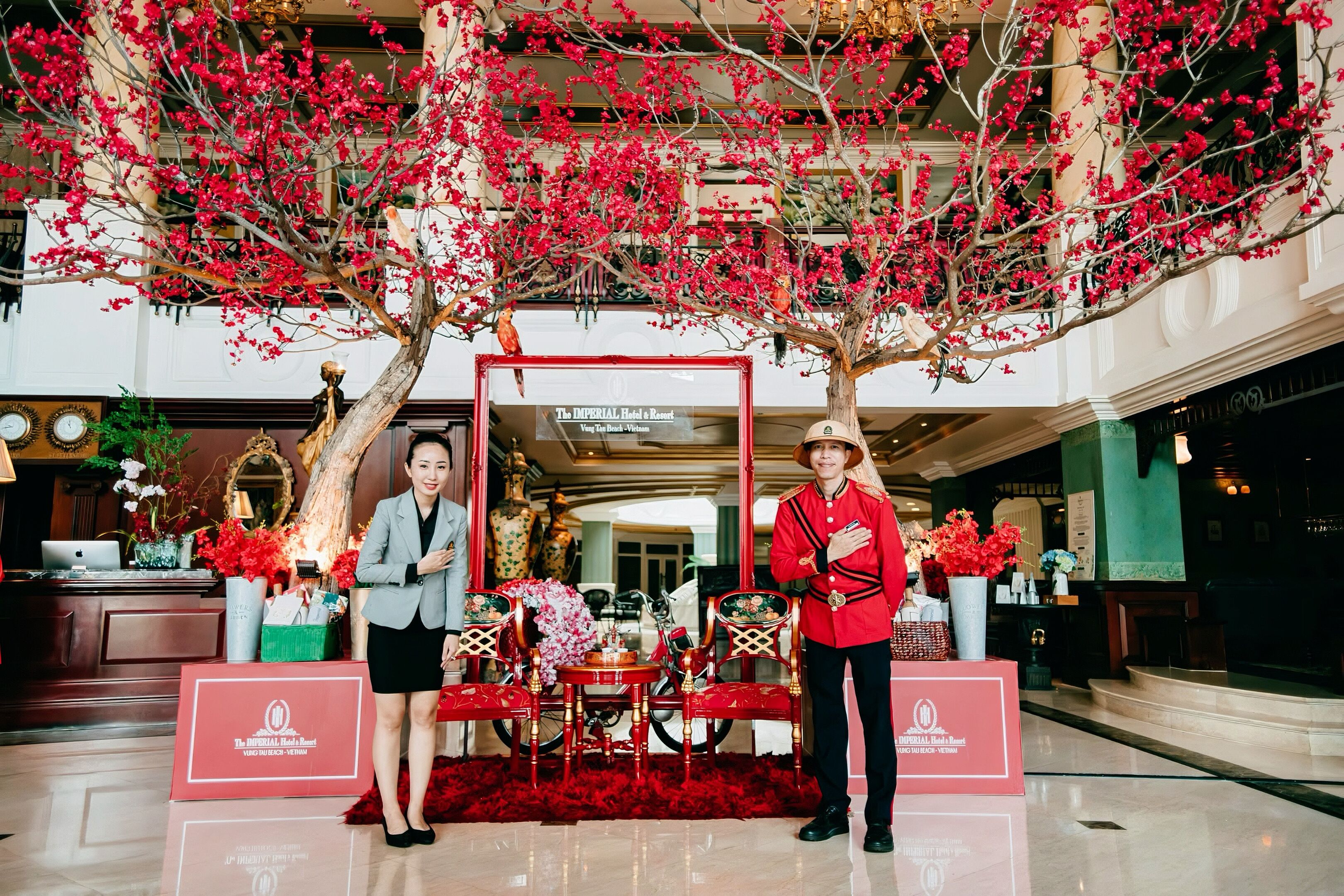 A reception area with a red floral arrangement, a reception desk, and a sign for The Imperial Hotel & Resort.