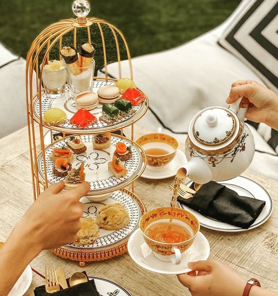 A three-tiered dessert stand with various pastries and a teapot on a table.