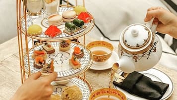 A three-tiered dessert stand with various pastries and a teapot on a table.