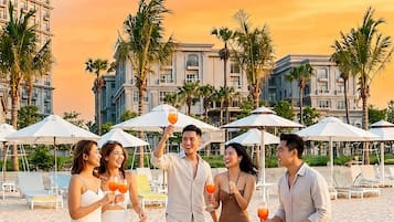 Un grupo de personas en la playa, con sombrillas y palmeras al fondo.