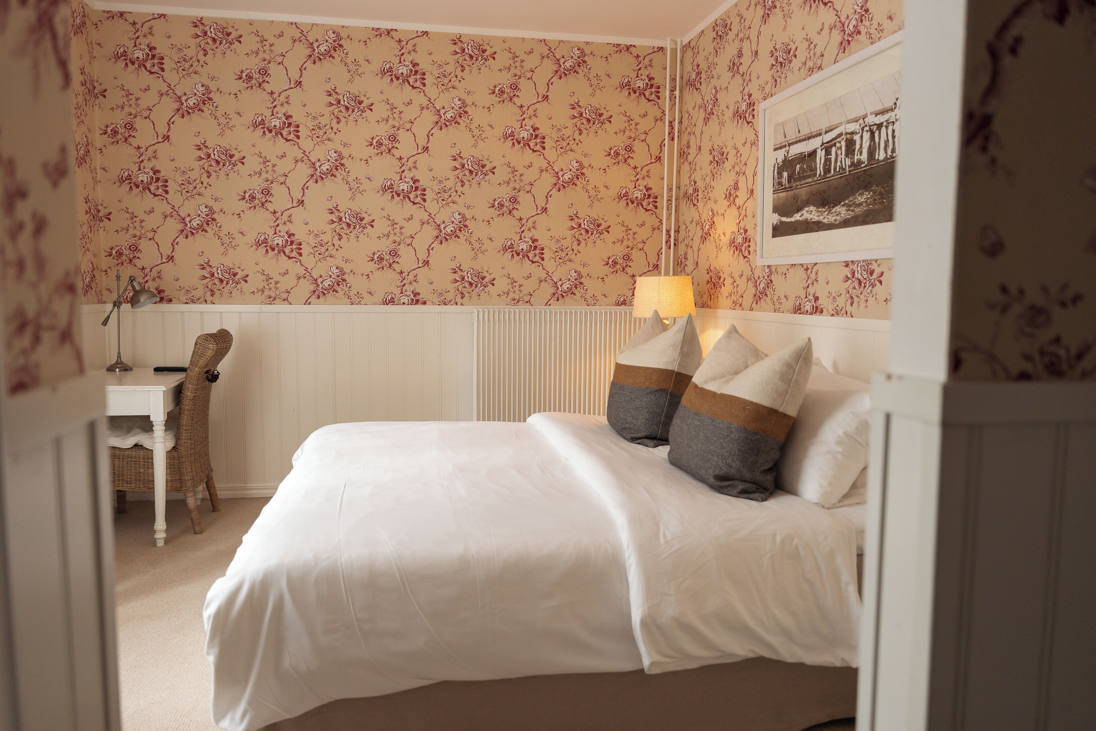 A bedroom with a bed, pillows, a desk, a chair, and a lamp.