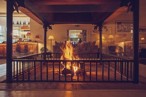 Un ambiente cálido y acogedor con chimenea, mobiliario de madera y una zona de bar al fondo.