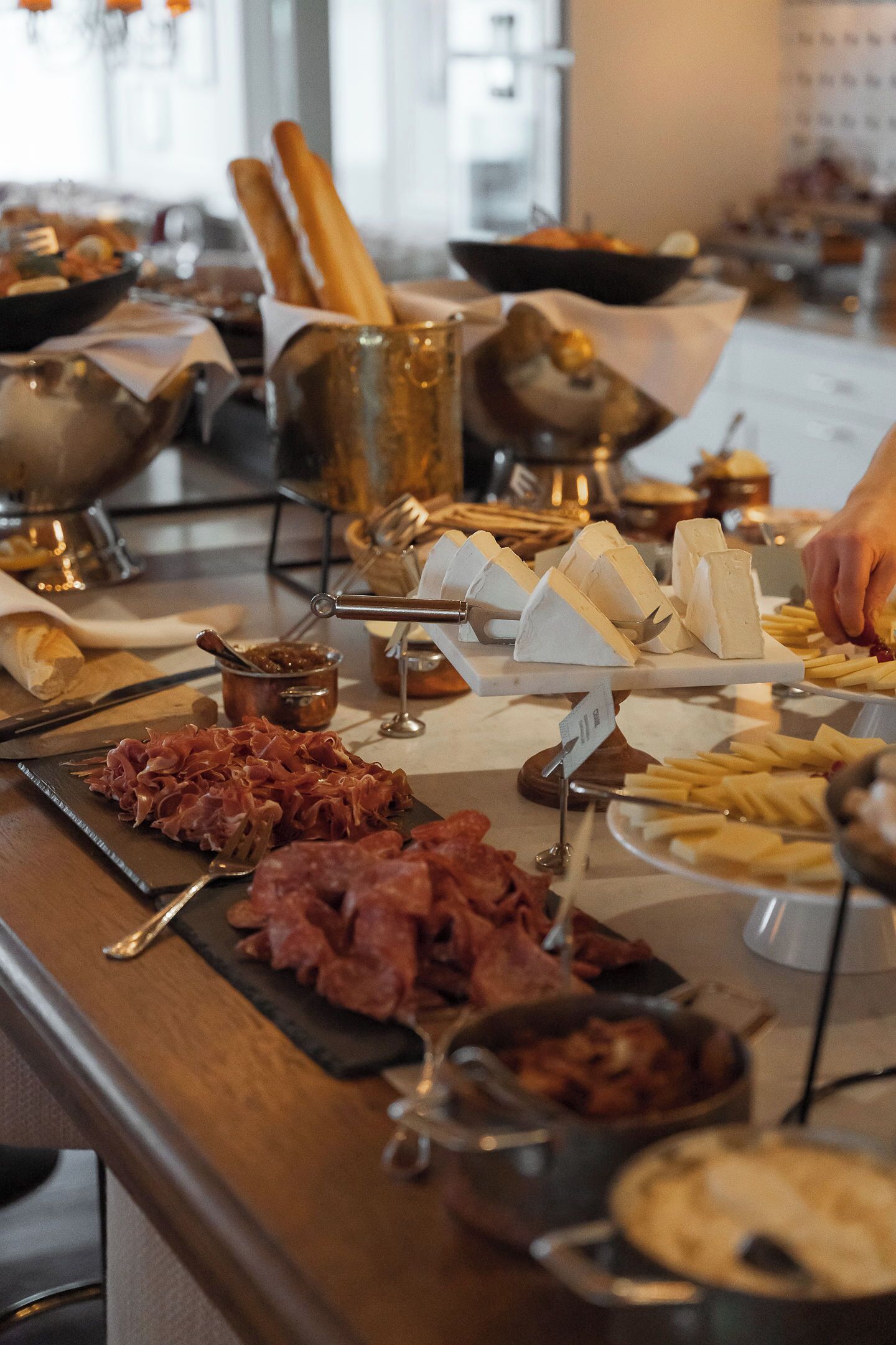 A buffet with various cheeses, meats, and bread.