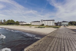 A beachside hotel with a wooden boardwalk leading to the beach, featuring multiple buildings with large windows and a sandy shoreline. - Ystad Saltsjöbad (Ystad)