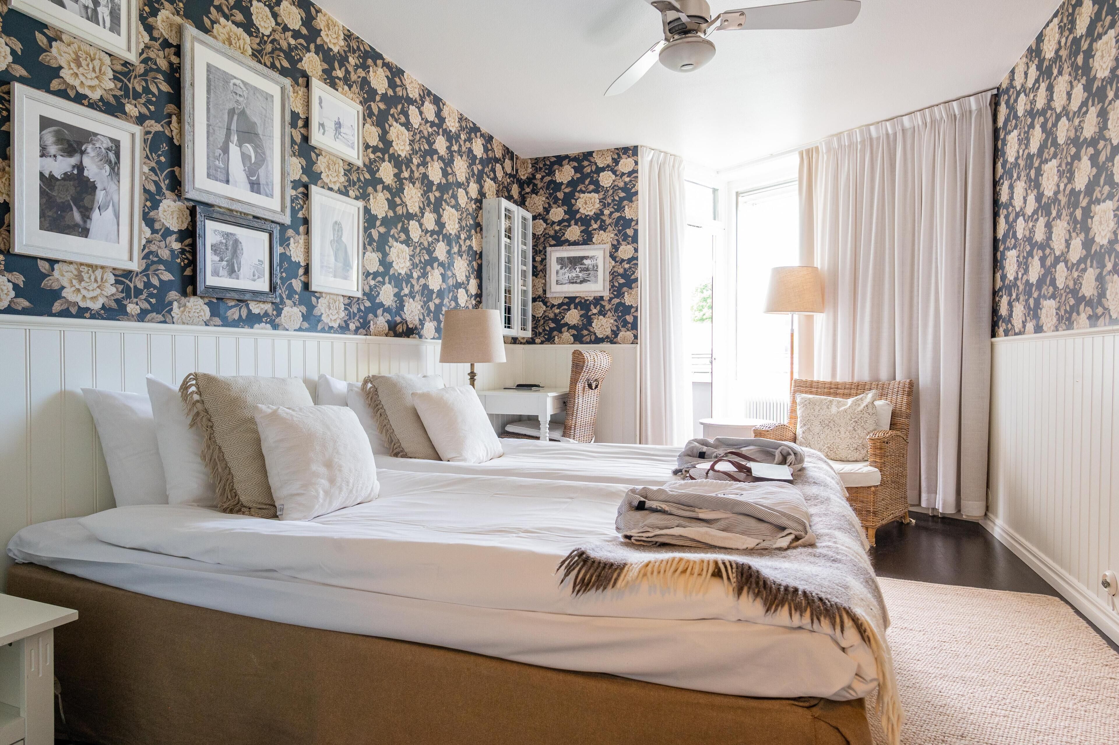 A bedroom with two beds, a white nightstand, a wicker chair, and a ceiling fan.