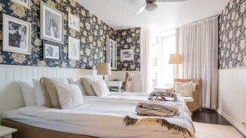 A bedroom with two beds, a white nightstand, a wicker chair, and a ceiling fan.