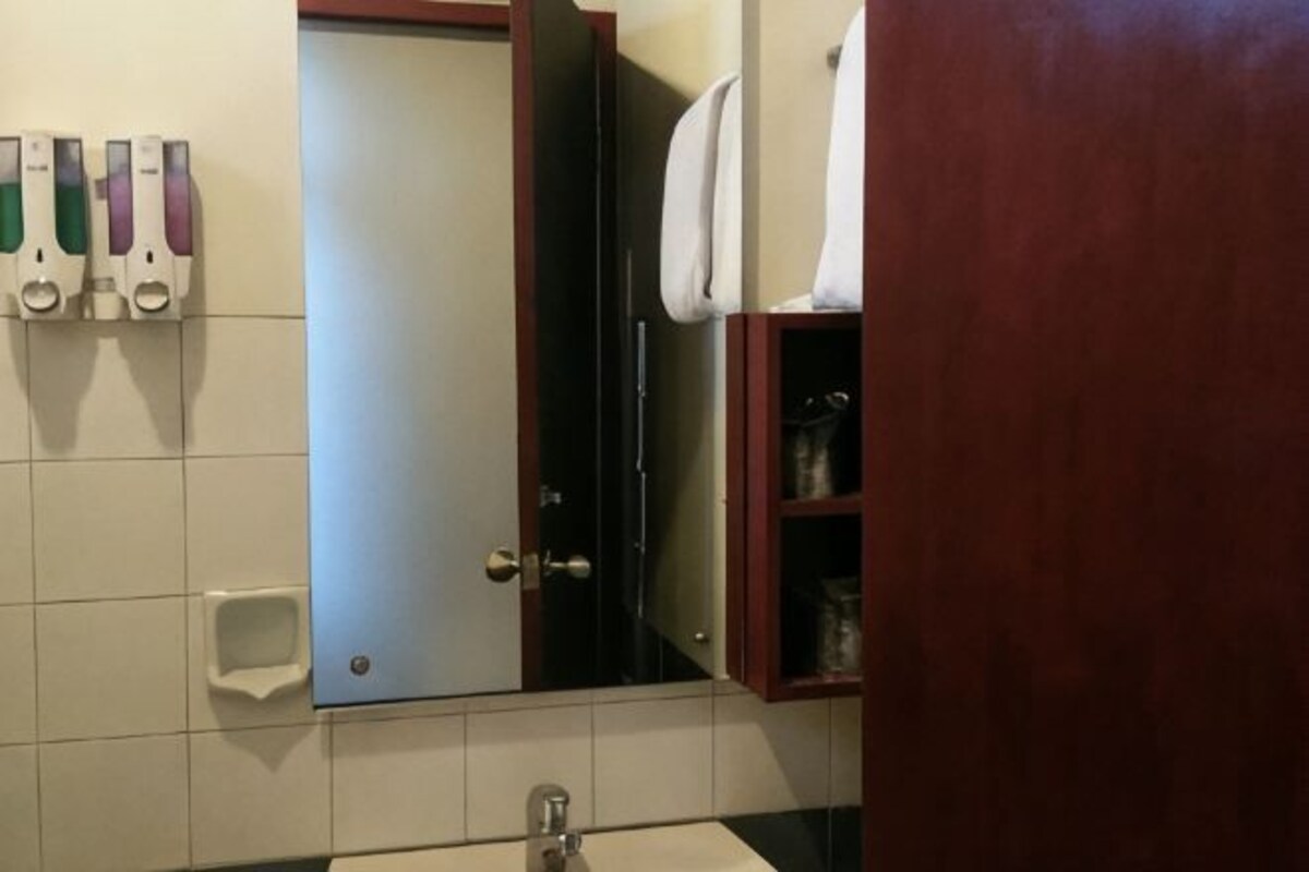 Un baño con lavamanos, espejo y dispensadores de jabón.