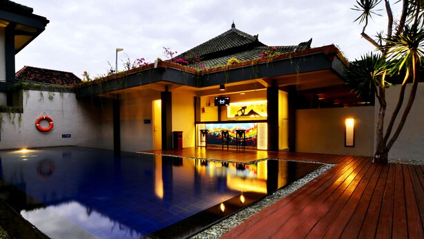 A swimming pool with a wooden deck, a lifebuoy, and a building with a tiled roof. - The Yani Hotel Bali (Denpasar)