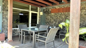 An outdoor patio with wicker furniture, a stone wall, and a wooden deck. - The Yani Hotel Bali (Denpasar)