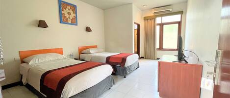 A hotel room with two beds, a desk, a TV, and a window with curtains.