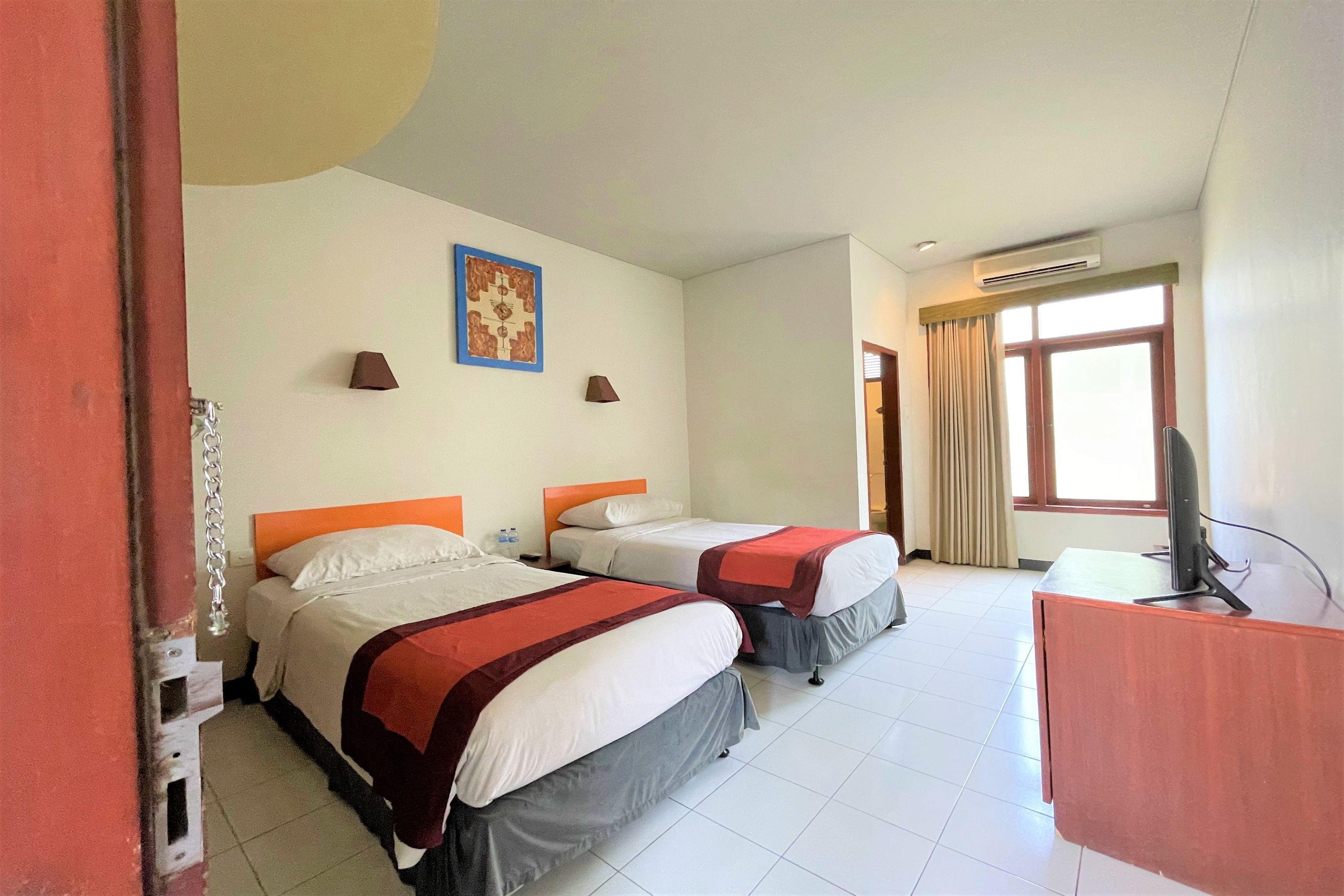 A hotel room with two beds, a desk, a television, and a window with curtains.