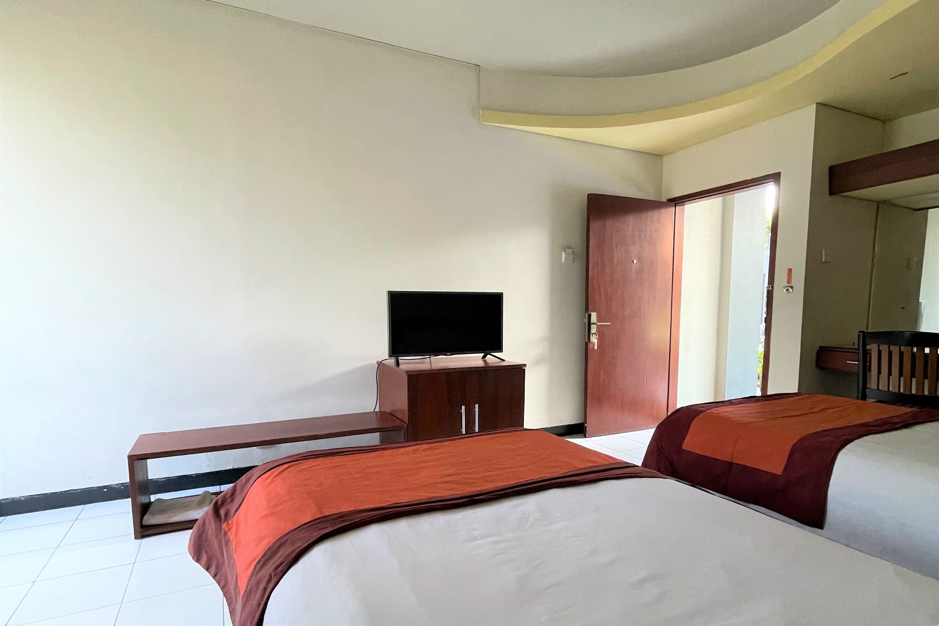 Camera d'albergo con due letti, una televisione su un mobile in legno e una porta che conduce a un'altra stanza.