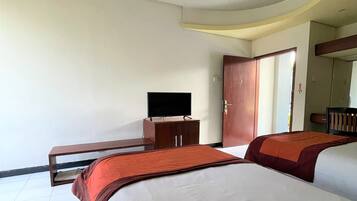 Camera d'albergo con due letti, una televisione su un mobile in legno e una porta che conduce a un'altra stanza.