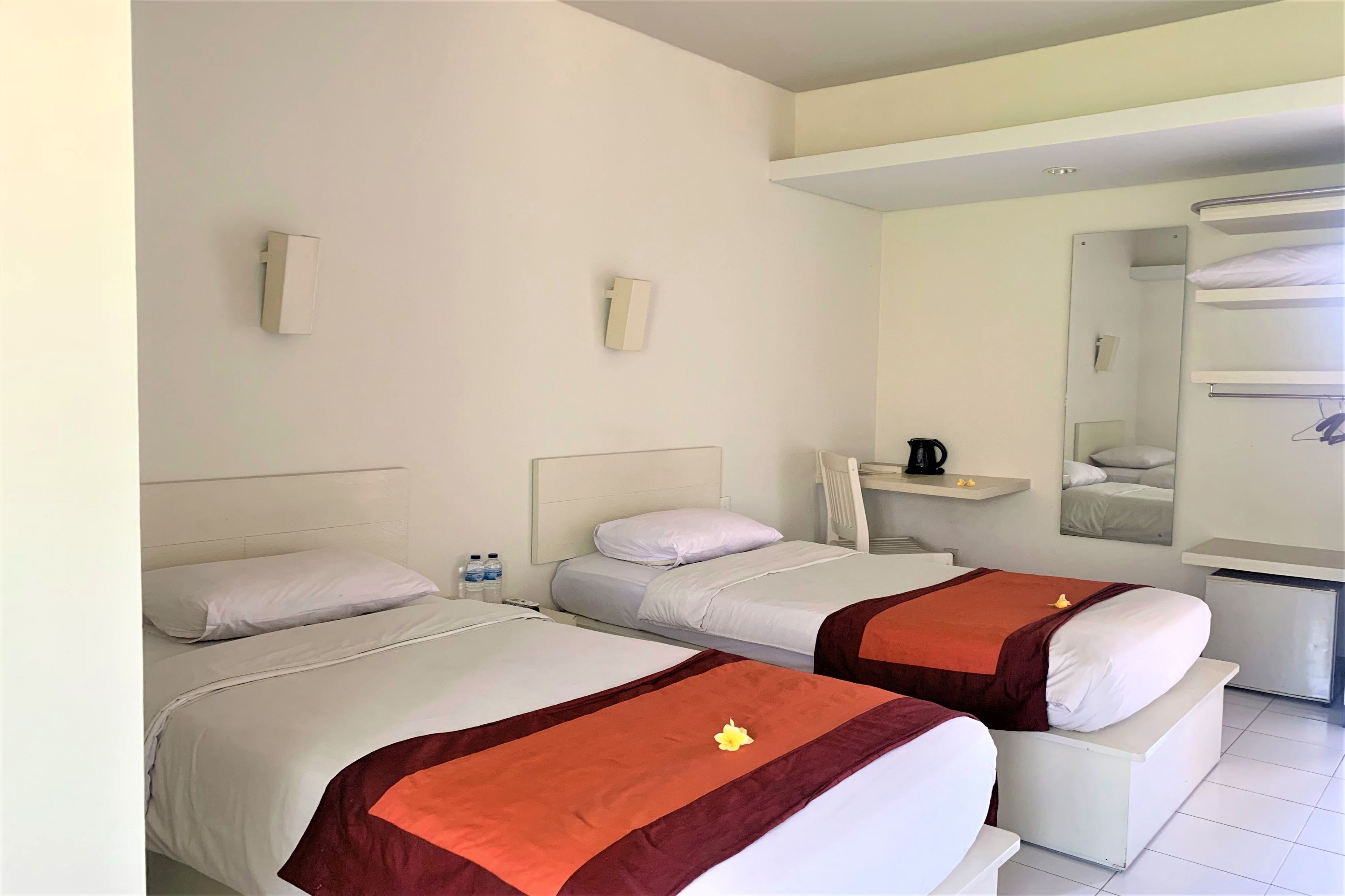 Habitación de hotel con dos camas, un escritorio pequeño, un espejo y un refrigerador minibar.