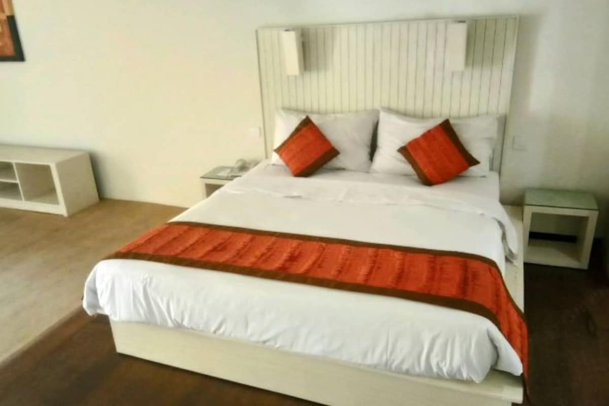 Una cama bien hecha con ropa de cama blanca y naranja, un cabecero de madera y una mesita de noche con una lámpara.