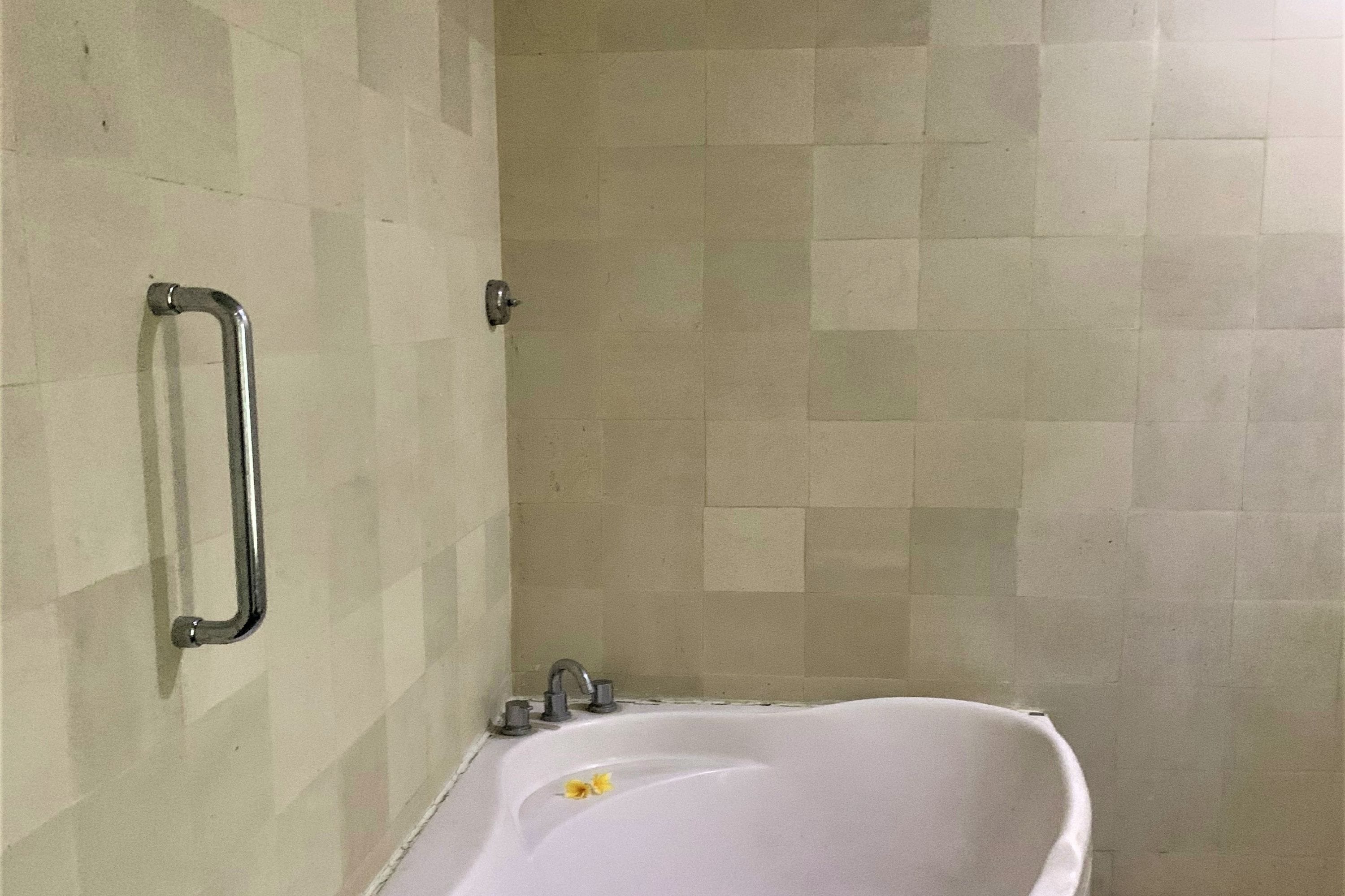 A bathroom with a white bathtub, a grab bar, and a shower area.
